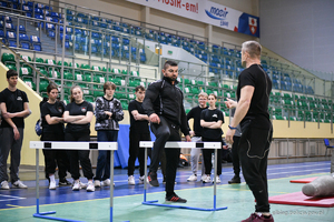 Policyjny instruktor w stroju sportowym tłumaczy kandydatom zasady toru sprawnościowego