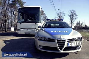 Oznakowany policyjny radiowóz. W tle autobus wycieczkowy. Zdjęcie stanowi ilustrację do tekstu.