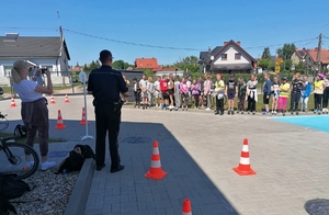 Umundurowany policjant stoi na placu. W tle grupa dzieci.