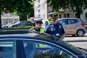 Umundurowana policjantka ruchu drogowego oraz umundurowany strażnik miejski stoją przy kontrolowanym samochodzie i rozmawiają z kierowcą.