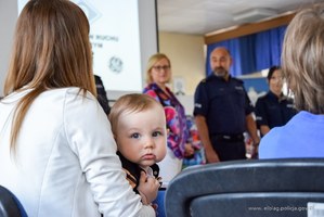 Mały chłopiec na rekach mamy, w tle policjanci