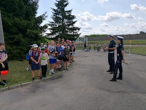 Umundurowani policjanci z ruchu drogowego stoja na placu manewrowym z grupa dzieci z rowerami.
