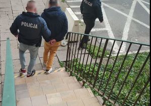 Policjanci operacyjni w niebieskich kurtkach oraz mężczyzna w kajdankach