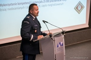 Umundurowany policjant przy mównicy. To nadinspektor Toamsz Klimek, Komendant Wojewódzki Policji w Olsztynie.