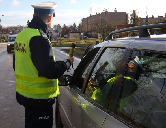 Umundurowany policjant stoi przy zatrzymanym samochodzie.