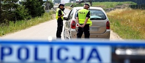 Umundurowani policjanci stoja przy zatrzymanym samochodzie.