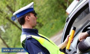 umundurowany policjant ruchu drogowego trzyma w ręku alkomat i bada nim trzeźwość kierującego