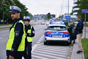 Umundurowani policjanci ruchu drogowego stoją na ulicy i kontrolują pojazdy. W tle oznakowany policyjny radiowóz. Zdjęcie jest ilustracja do tekstu weekend na elbląskich drogach: pijany traktorzysta z dożywotnim zakazem zatrzymany.