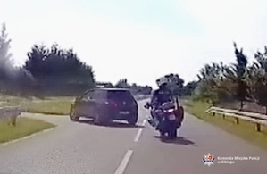 Policyjny oznakowany motocykl jedzie za uciekającym volkswagenem