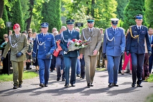 Umundurowani przedstawiciele służb składają kwiaty na cmentarzu.
