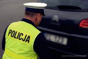Policjant patrzy na tablice rejestracyjną  zatrzymanego samochodu