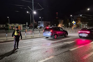 umundurowany policjant stoi na jezdni i kontroluje przejeżdżające samochody